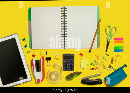 multiple school and office suplies and gadgets lying on a yellow background Stock Photo