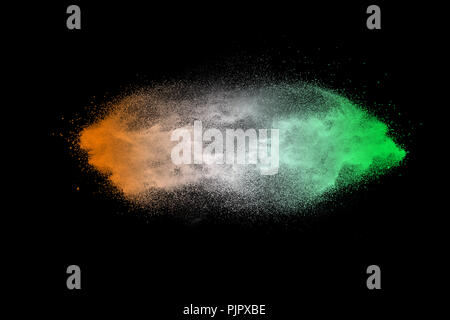 Green orange dust particles explosion on black background. Color powder dust splash. Stock Photo