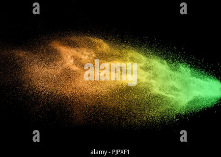 Green orange dust particles explosion on black background. Color powder dust splash. Stock Photo