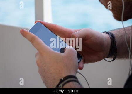 close up mobile phone in hands a young hipster trendy dressed Young man on a background of a stone paving slabs and blur brick. Young man typing on mo Stock Photo