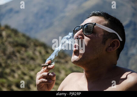 Young man smoking tobacco, man with sunglasses and mountains background Stock Photo