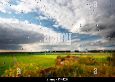 Green landscape shortly after the rain, seen through a window still covered with raindrops. Stock Photo