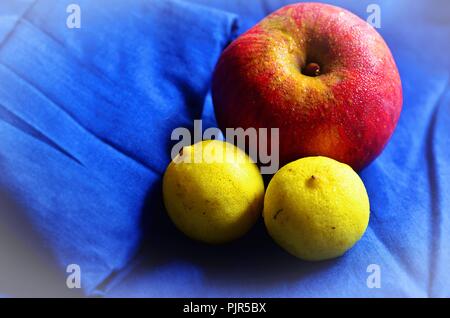 Red sweating apple with two ripe lemons, kept on a blue shirt Stock Photo