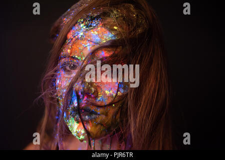 Studio headshot of a woman's face covered in coloured powder under an ultra violet light Stock Photo