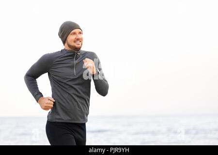 portrait of running smiling man in sportswear and hat against sea background Stock Photo