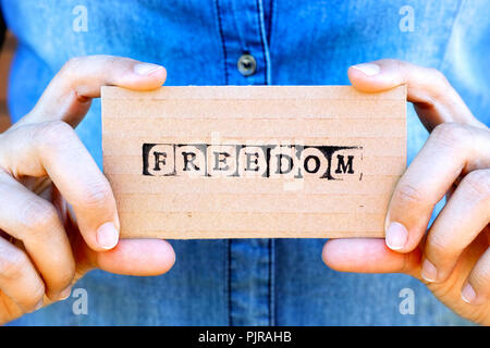 Woman hand holding cardboard card with word Freedom made by black alphabet stamps. Denim backgrounds. Stock Photo
