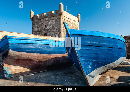two blue fishing boats are stranded on a dock at the foot of the citadel of Mogador in Essaouira in Morocco Stock Photo