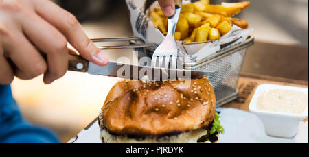 Girl cutting a burger in the restaurant close up Stock Photo