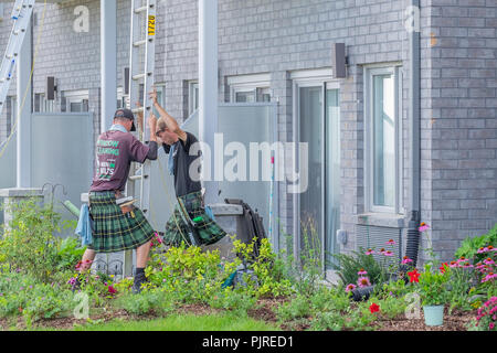 Windows cleaning crew wearing kilts set a ladder in place at a job site. Stock Photo