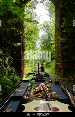 Woman steering a narrowboat going through a high bridge on the Shropshire Union canal near Market Drayton Stock Photo