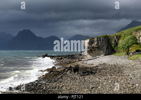 Rocky shore at Port na Cullaidh harbour Elgol with Red Cuillin Mountains under clouds at Loch Scavaig Isle of Skye Scotland UK Stock Photo