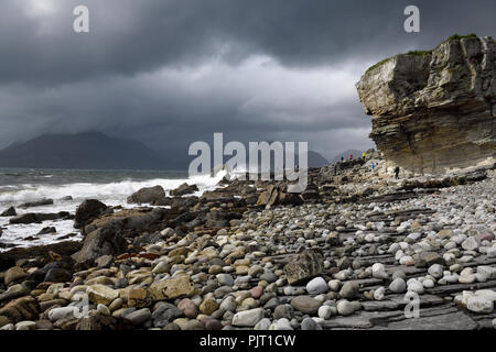 Tourists on rocks of Elgol beach at Port na Cullaidh with Red Cuillin Mountains under clouds on Loch Scavaig Isle of Skye Scotland UK Stock Photo