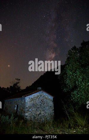 Stars and milky way with shiny star over the old watermill building and olive green tree in front of green plants Stock Photo