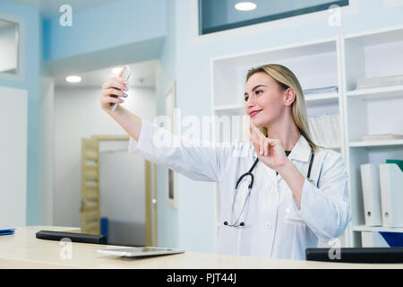 Smiling nurse taking selfies with her phone behind reception desk Stock Photo