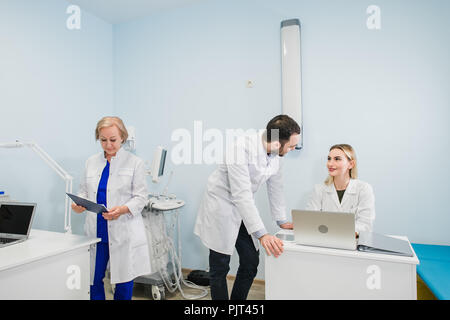 Photo of three doctors together discussing new way of treatment while having a meeting at office. Doctors using laptop computer while discussing new way of treatment. Stock Photo