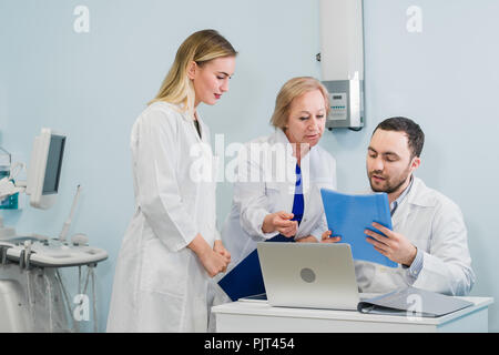 Photo of three doctors together discussing new way of treatment while having a meeting at office. Doctors using laptop computer while discussing new way of treatment. Stock Photo