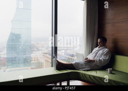 Happy man drinking coffee and using laptop in bed in the morning Stock Photo