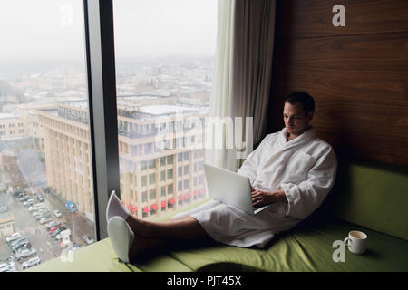 Happy man drinking coffee and using laptop in bed in the morning Stock Photo