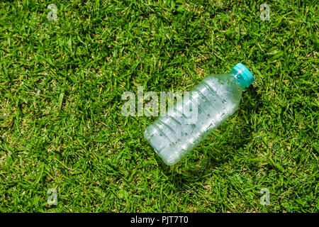 Small cold water bottle laying on green grassy field on a hot sunny day with room for copy space, good for health or sport concept Stock Photo