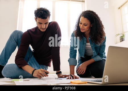 Business man and woman working together sitting on the floor in office with papers lying on the floor. Business colleagues sitting on the floor and lo Stock Photo