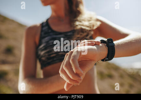 Female runner checking fitness progress on her smart watch. Close up of woman using fitness app to monitor workout performance, while training on moun Stock Photo