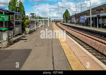 Two of the platforms and rail tracks at Motherwell Station in North Lanarkshire, Scotland. Two waiting pasengers, seats, car park, recycling bins, clo Stock Photo