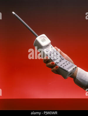 1991 HISTORICAL WOMANS HAND HOLDING UP CORDLESS TELEPHONE (©SONY CORP 1990) ON PLAIN RED BACKGROUND Stock Photo
