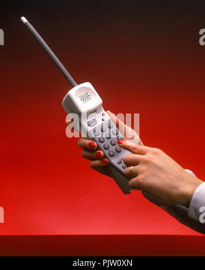 1991 HISTORICAL WOMANS HAND DIALING CORDLESS TELEPHONE (©SONY CORP 1990) ON PLAIN RED BACKGROUND Stock Photo