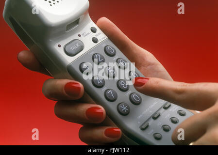 1991 HISTORICAL WOMANS HAND DIALING CORDLESS TELEPHONE (©SONY CORP 1990) ON PLAIN RED BACKGROUND Stock Photo