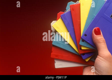 1991 HISTORICAL WOMAN’S HAND HOLDING MULTICOLORED 3.5 INCH MICRO FLOPPY DISCS (©IBM CORP 1973) ON PLAIN RED BACKGROUND Stock Photo