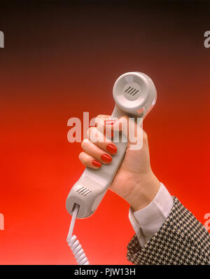 1991 HISTORICAL WOMANS HAND HOLDING UP LANDLINE TELEPHONE (©SONY CORP 1990) ON PLAIN RED BACKGROUND Stock Photo