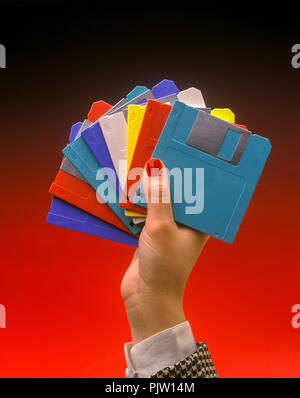 1991 HISTORICAL WOMAN’S HAND HOLDING MULTICOLORED 3.5 INCH MICRO FLOPPY DISCS (©IBM CORP 1973) ON PLAIN RED BACKGROUND Stock Photo