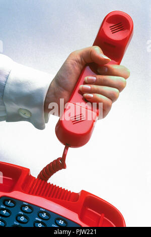 1991 HISTORICAL WOMANS HAND HOLDING UP RED LANDLINE TELEPHONE ON PLAIN RED BACKGROUND Stock Photo