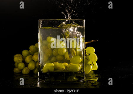 a bunch of grapes on a black background. jar of water splash from falling berries. Stock Photo