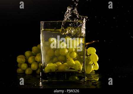 a bunch of grapes on a black background. jar of water splash from falling berries. Stock Photo