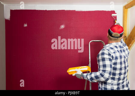 Home improvement. A man in a red hat coloring a room with a paint roller and paint brush. Stock Photo