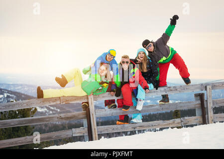 Group of happy friends is having fun at ski resort against sunset mountains