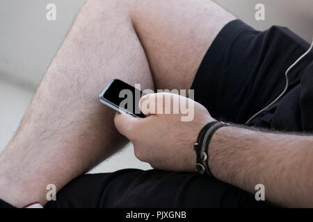 close up mobile phone in hands a young hipster trendy dressed Young man on a background of a stone paving slabs and blur brick. Young man typing on mo Stock Photo