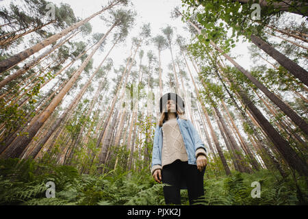 Young woman standing in forest with high trees Stock Photo