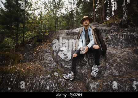 Young man sitting on cliff in forest Stock Photo