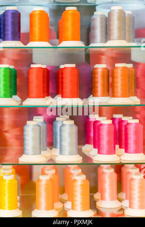 Background with a lot of colorful coils with threads. Bobbins are stacked in three rows, one on the other. The winding is erratic. Multicolored thread Stock Photo