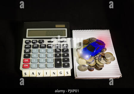 Saving money concept, a car above the pile of coins beside a calculator Stock Photo