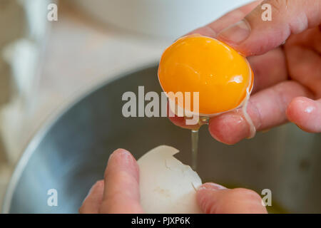Female hands separate the egg white from the yolk over a bowl in the kitchen. the cook separates the yolk in the egg. Stock Photo