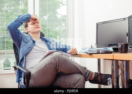 Frustrated young man feeling stressed after hard work, having tired expression, keeping his hand on eyes, resting for minute. Stock Photo