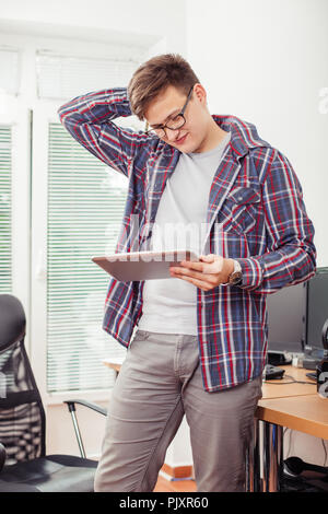Worried young man is reading e-mail on  digital tablet while sitading in his office. Stock Photo