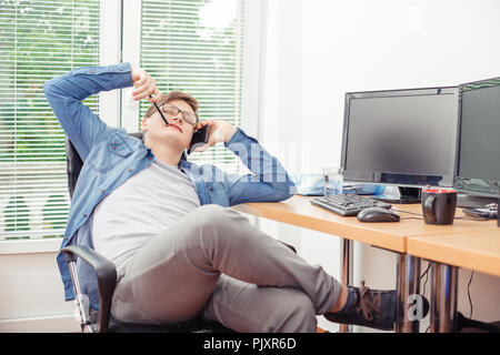 Handsome young man programmer talking on the mobile phone, resting and smiling while sitting at his working place in office Stock Photo
