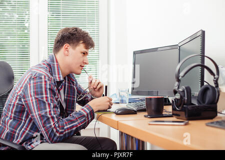 Shot of young man, graphic designer in casual clothes in the office, using graphics tablet to work at desk on a desktop computer. Stock Photo