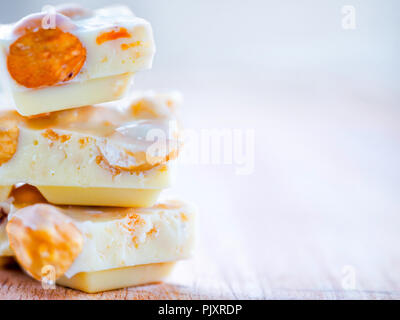 White chocolate with whole hazelnuts on wooden background close up. Few chocolate pieces with whole hazelnuts are stacked. Copy space Stock Photo