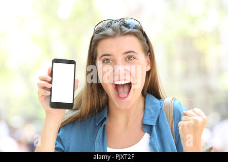 Front view portrait of a excited woman showing a smart phone screen mockup in the street Stock Photo