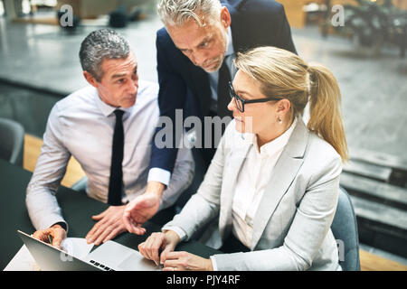 Mature manager and two executives working together on a laptop during a meeting in the lobby of a modern office Stock Photo